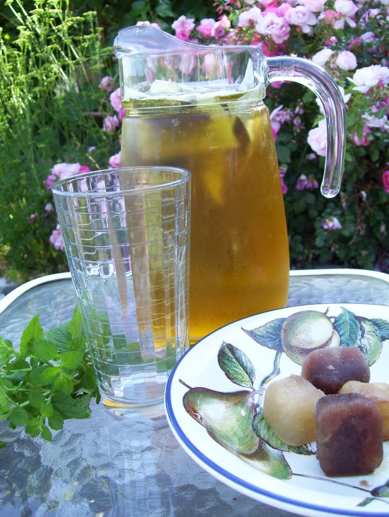 Pomegranate ice cubes in the foreground; Lemon balm sprigs to the side; my lovely rosebush in the background